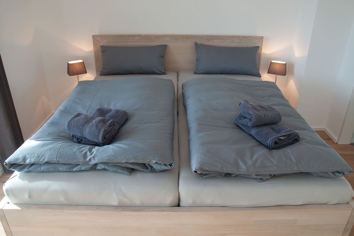 Cama de casal com duas almofadas e duas toalhas dobradas, com abajur de cada lado.