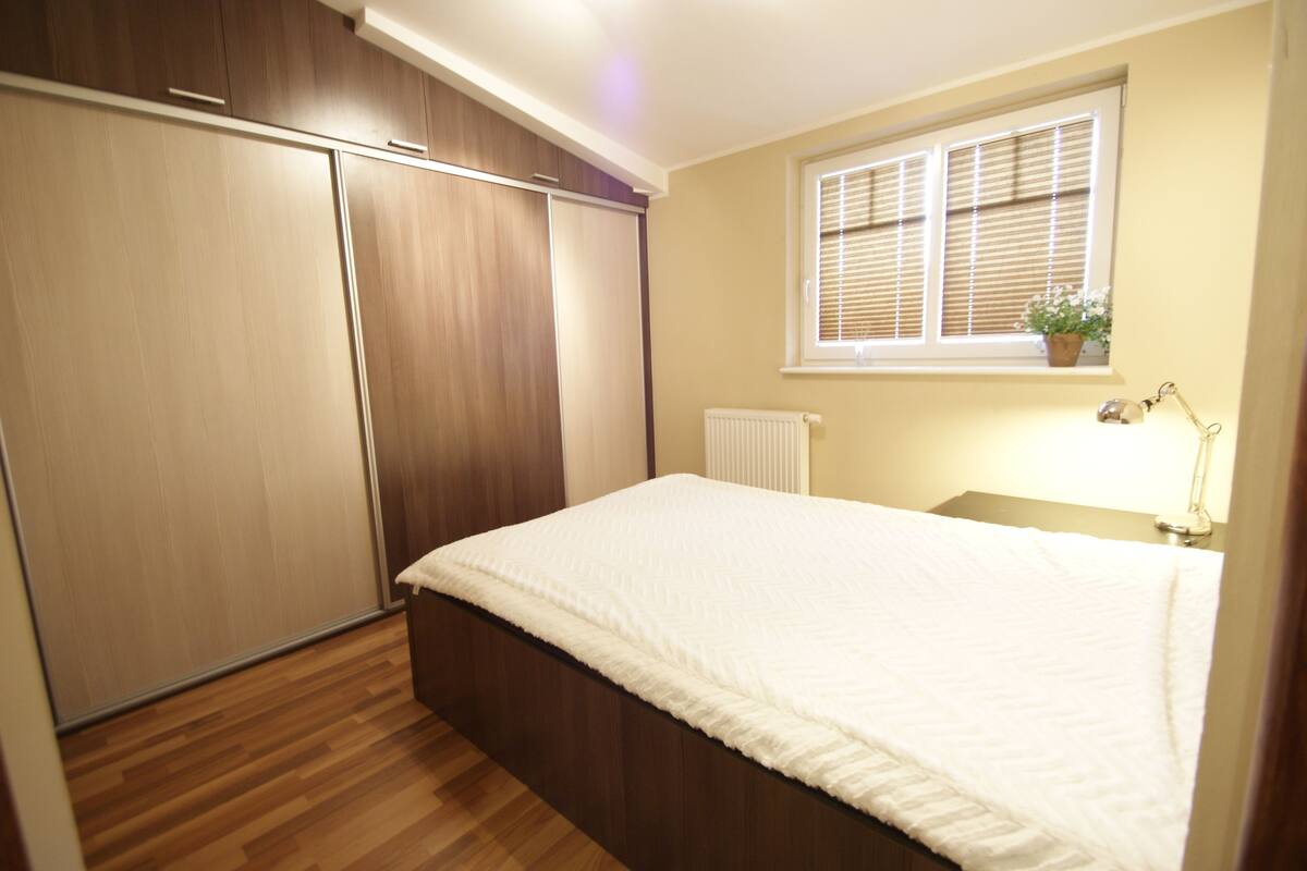 A bedroom with a bed, wooden wardrobe, and a window with blinds.