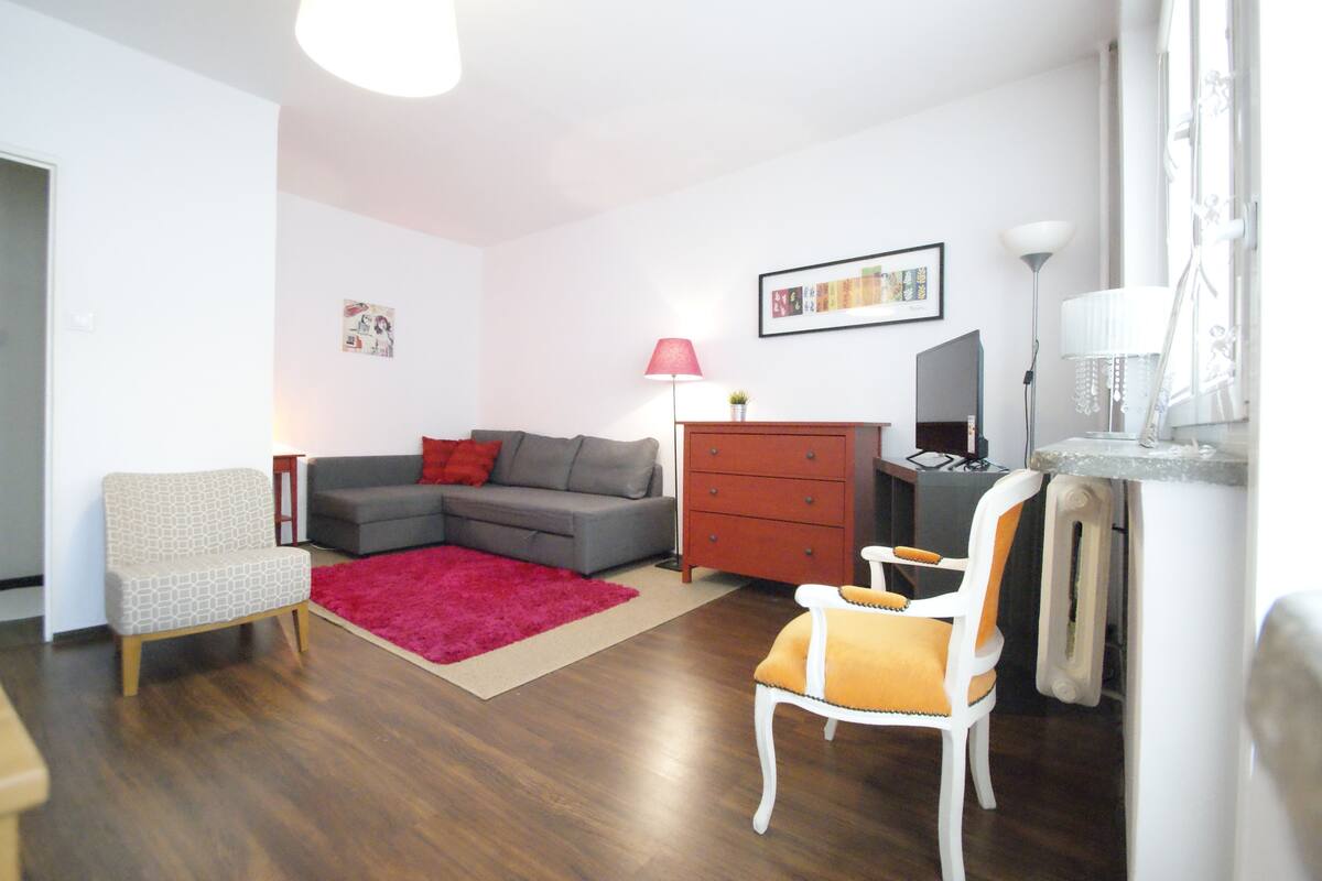 A modern living room with a grey sectional sofa, a red rug, a white armchair, and a small table with a lamp.