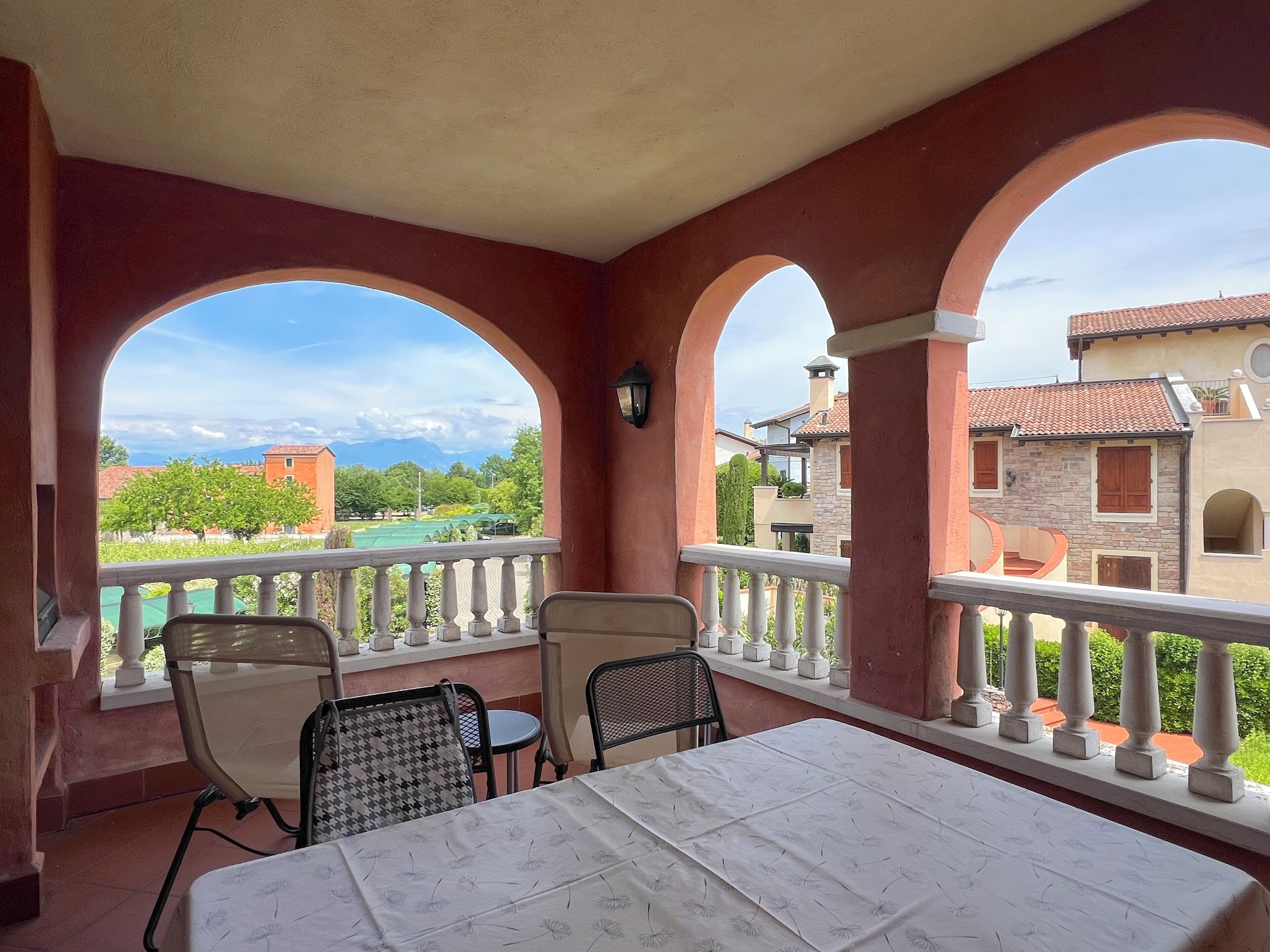 A balcony with a table and chairs, overlooking a scenic view of buildings and greenery.