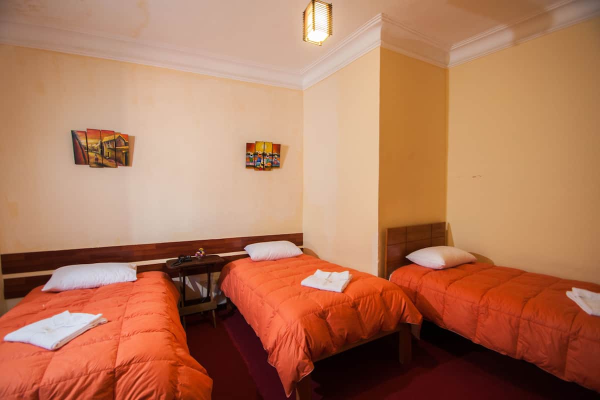 A hotel room with two beds, each with an orange bedspread and white pillows. There are two paintings on the wall, a nightstand, and a lamp.