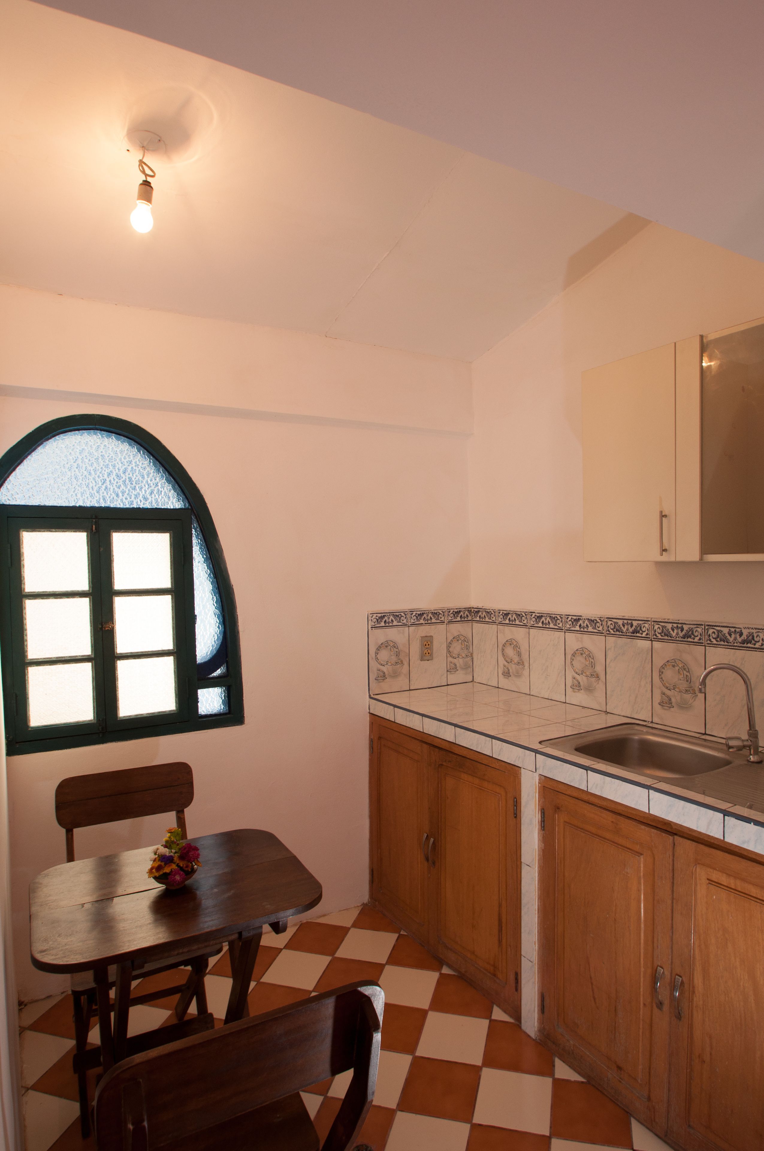 A kitchen with a checkered floor, wooden cabinets, a window with a green frame, and a table with chairs.