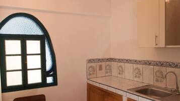 A kitchen with a checkered floor, wooden cabinets, a window with a green frame, and a table with chairs.