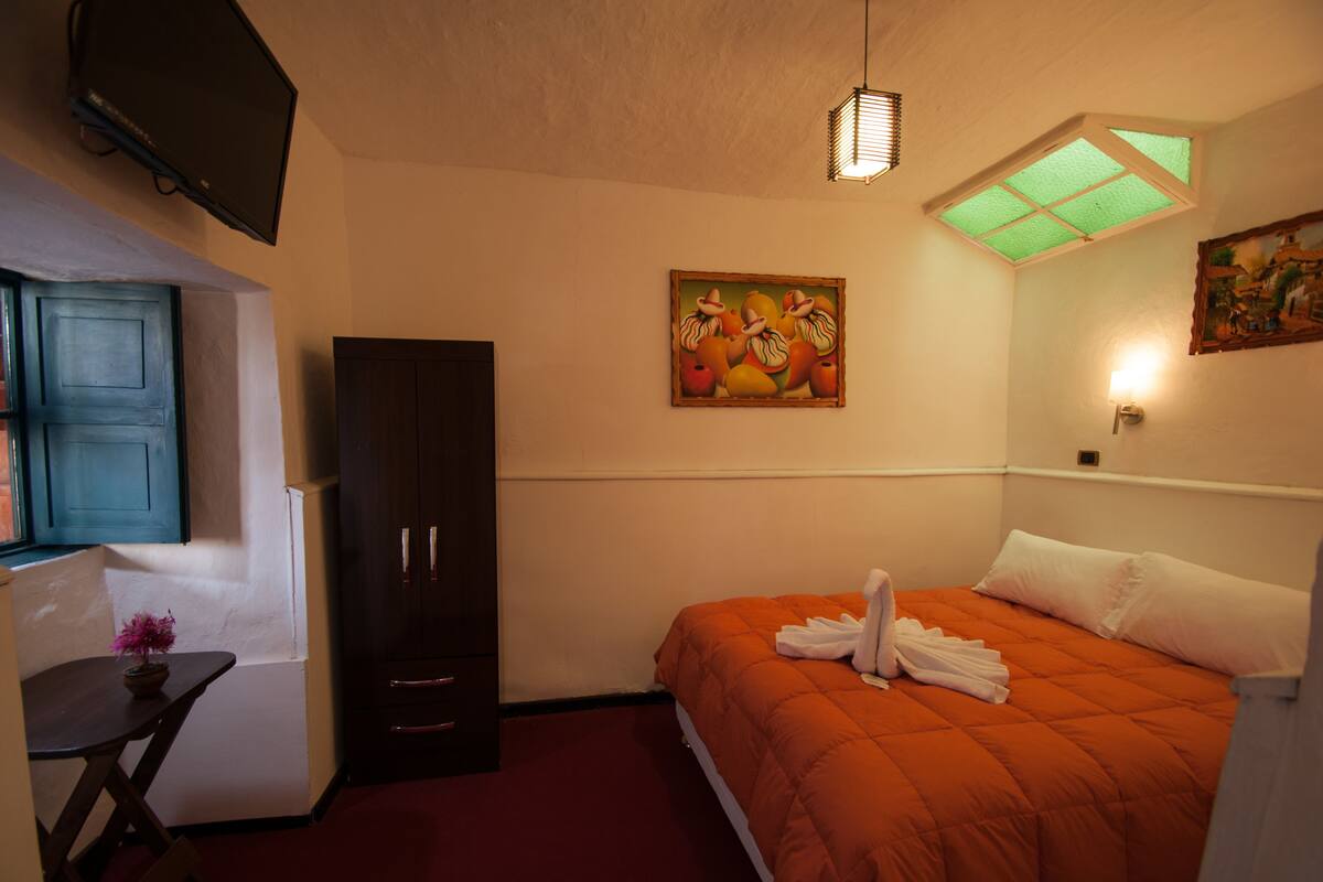 A hotel room with a bed, a desk, a wardrobe, a painting, and a ceiling light.