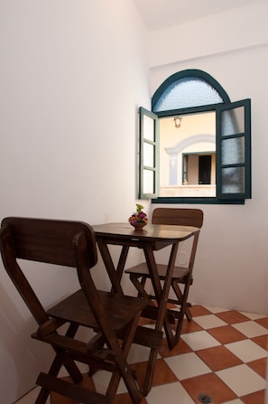Uma pequena área de refeições com uma mesa e duas cadeiras de madeira, uma janela com uma persiana aberta e piso de azulejos.