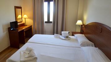Habitació d'hotel amb un llit, un escriptori amb làmpada, un mirall i una finestra amb cortines.