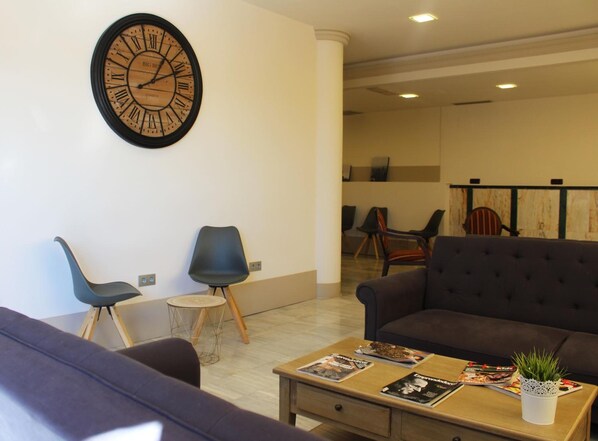 A modern living room with a large wall clock, a sofa, a coffee table with magazines, and a small side table.