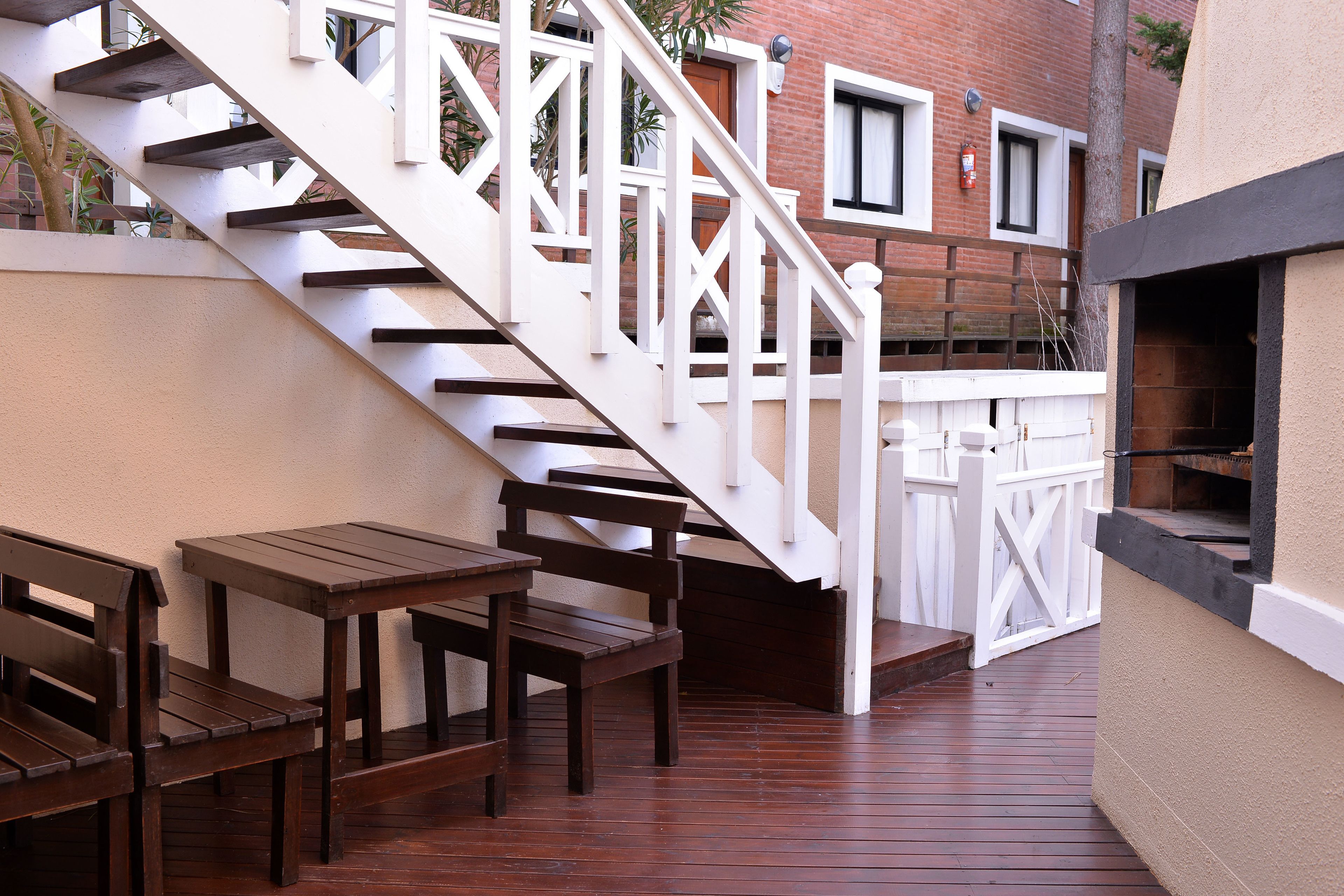 Una terraza de madera con escaleras blancas, bancos de madera y una parrilla.