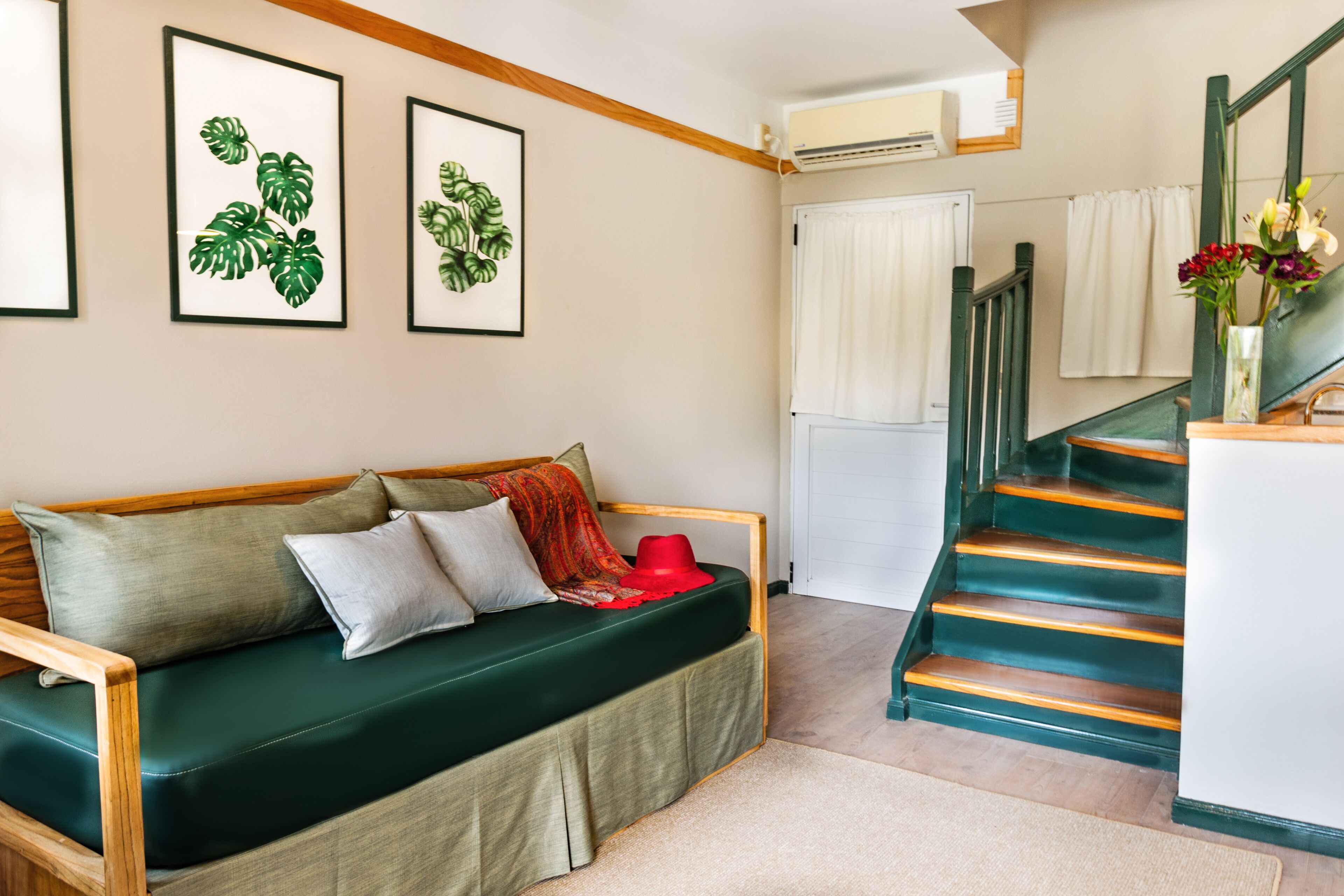 Ein Zimmer mit einem grünen Sofa, einer Holzbank, einer Treppe mit grünen Stufen und gerahmten Pflanzenbildern an der Wand.