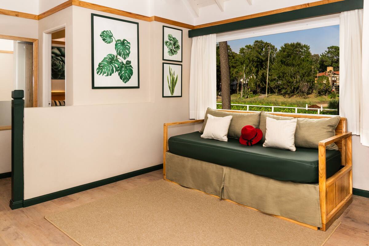 A room with a green sofa, a wooden bench, and a view of trees and buildings through a window.