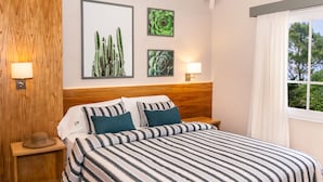 Una cama bien hecha con ropa de cama a rayas, dos lámparas fijadas a la pared y obras de arte botánicas enmarcadas en la pared.