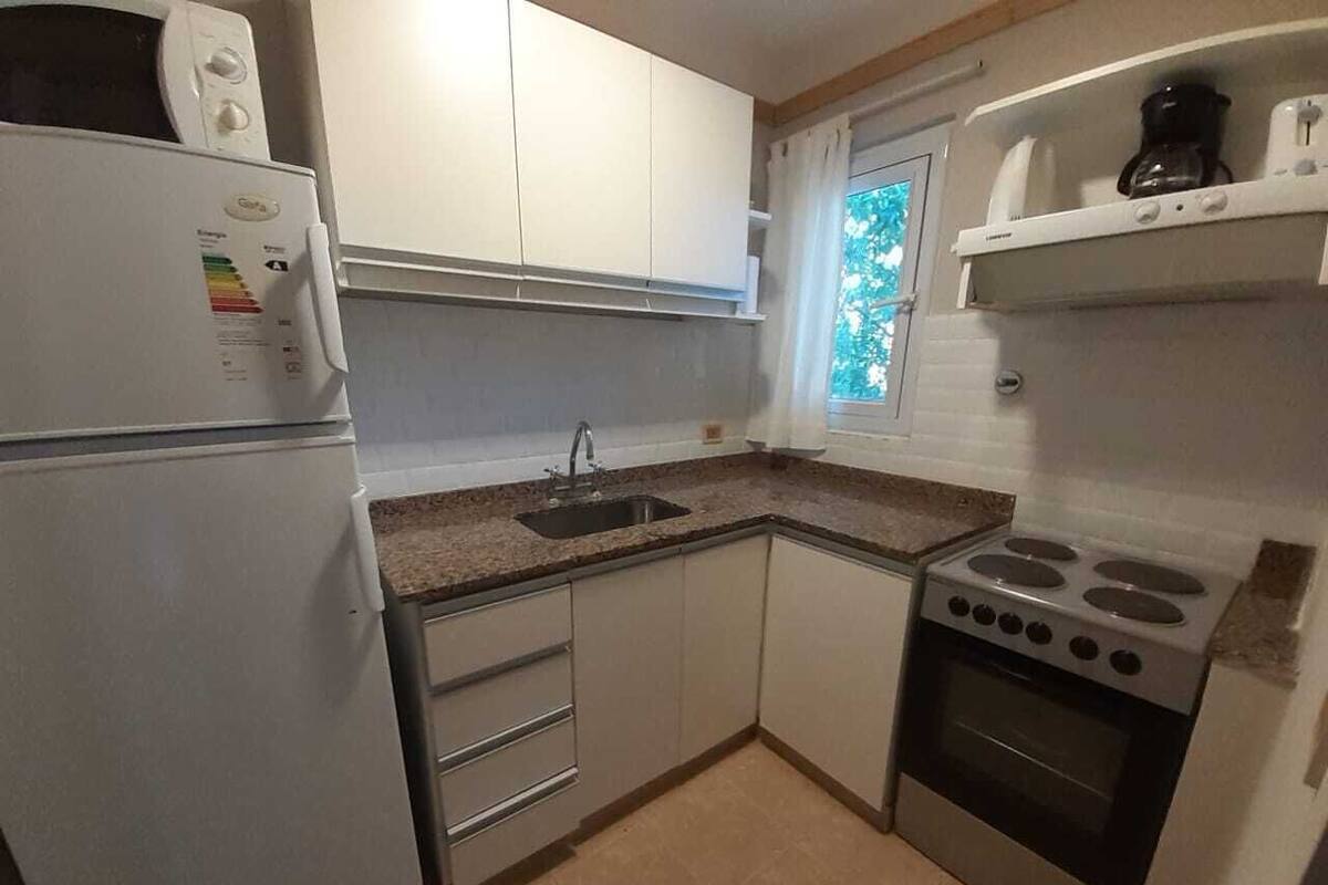 A compact kitchen with a refrigerator, sink, stove, and cabinets.