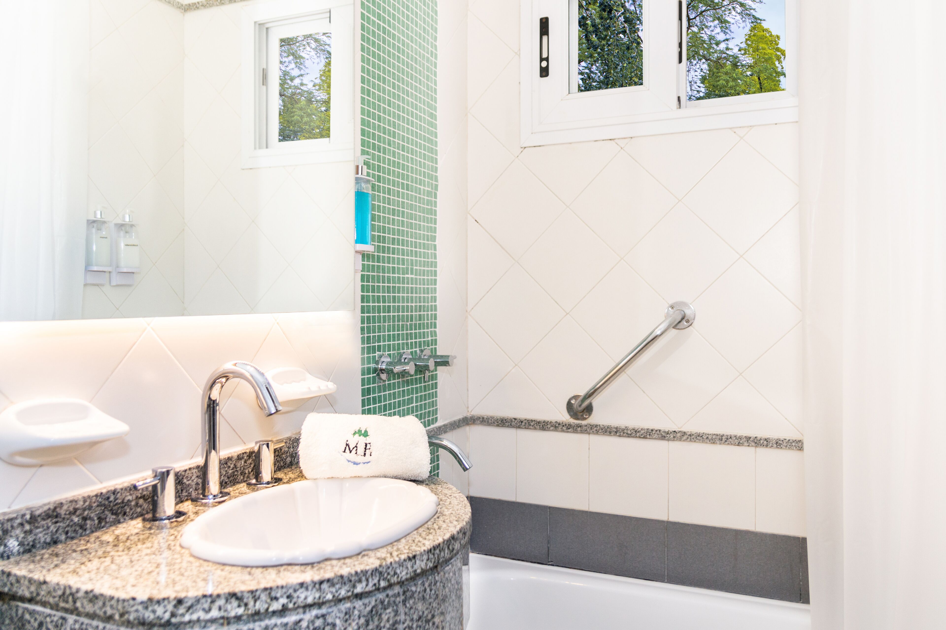 A bathroom with a granite countertop sink, a mirror, a window, and a shower with a grab bar.