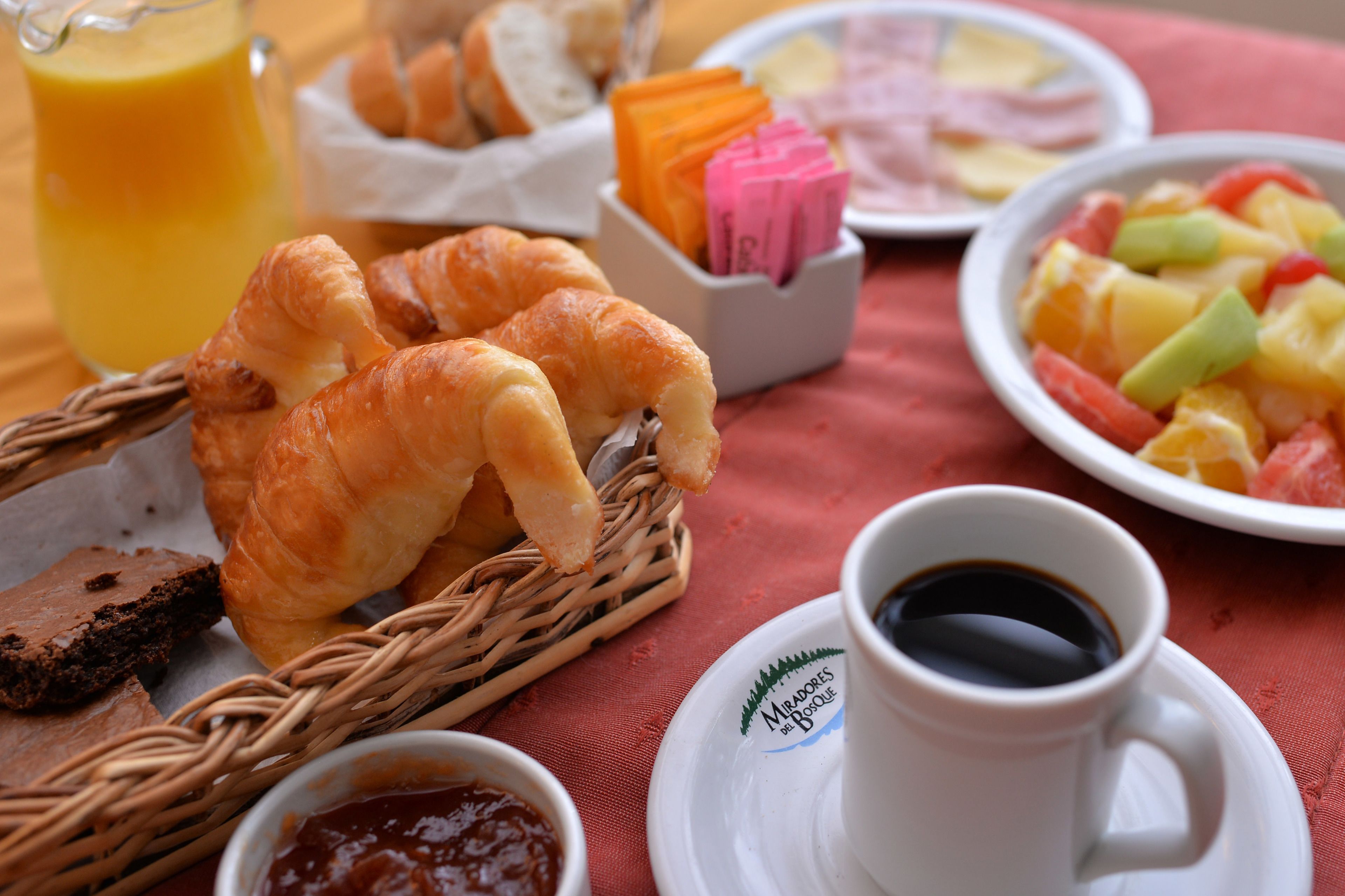 A breakfast setting with croissants, fruit salad, juice, and coffee.