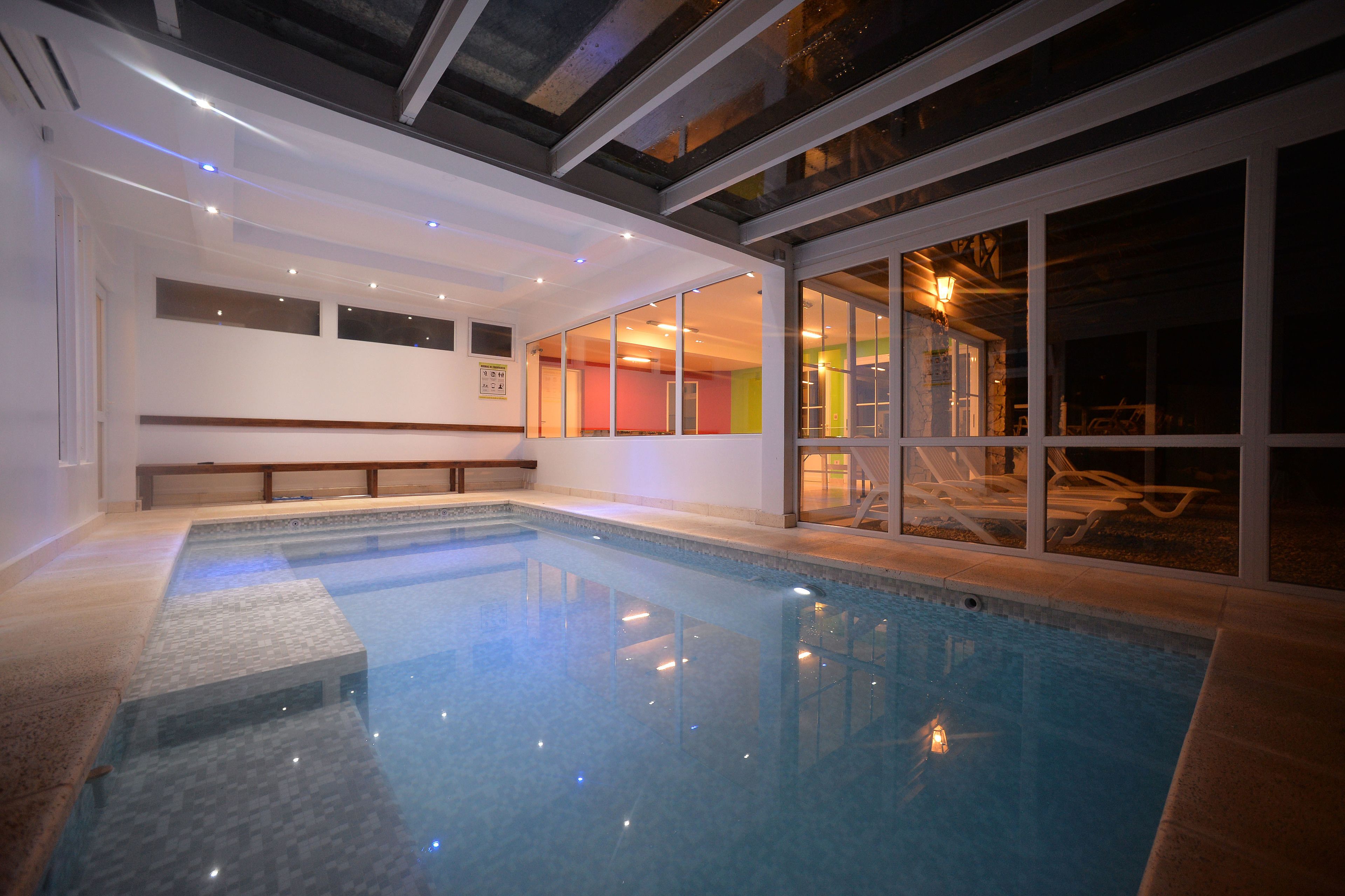 Una piscina interior con agua cristalina, una terraza de madera y un muro de vidrio con vistas al exterior.