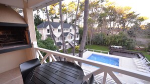 Un balcón con una mesa y sillas negras, con vistas a una piscina y una casa.