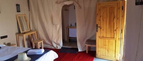 Un dormitorio con cama, una puerta de madera, un espejo y una mesita.
