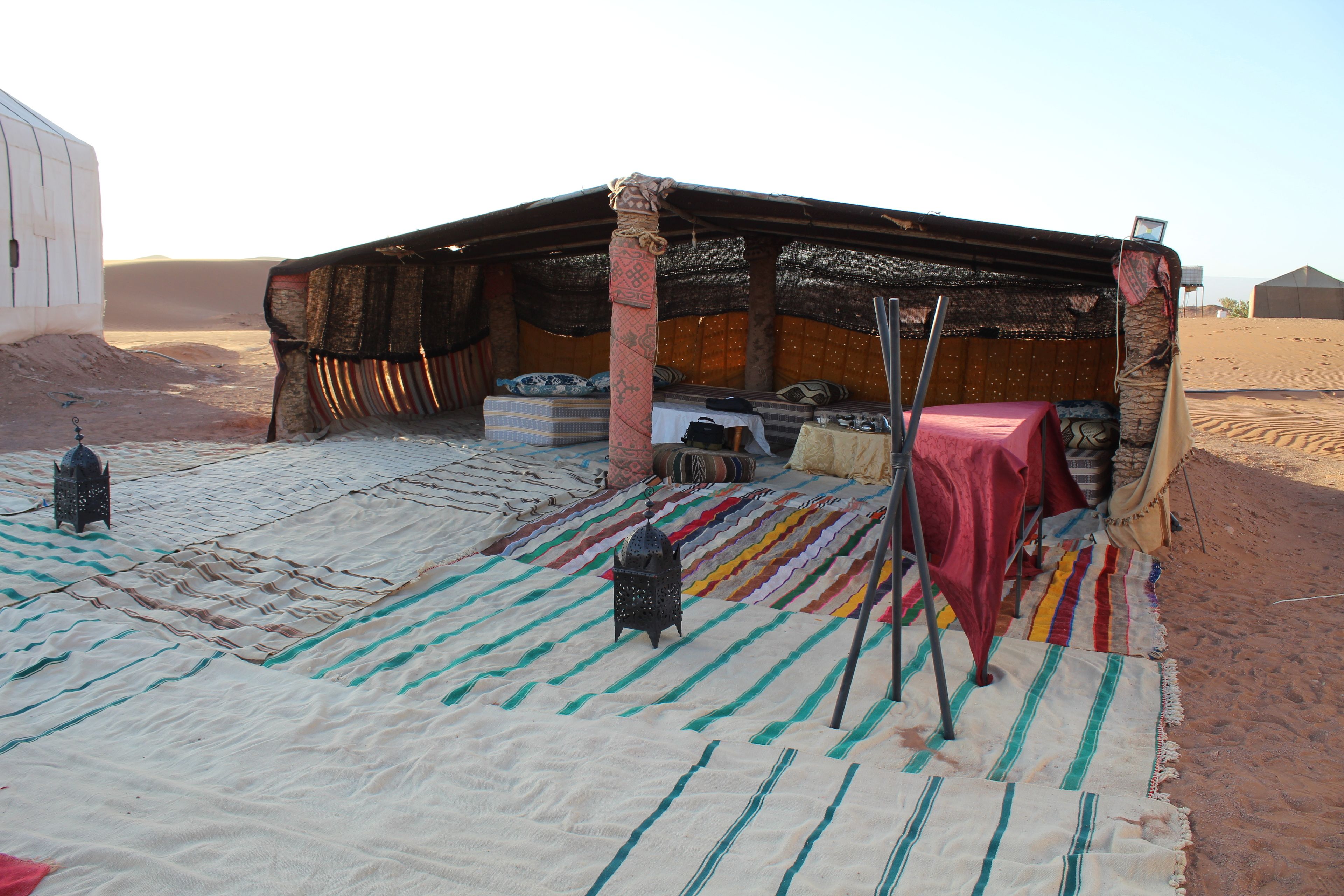 Een tentvormige constructie met een bed, kussens en een tafel bedekt met een rode doek.