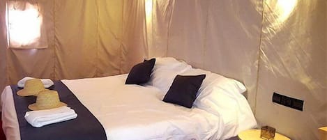 A single bed with white linens, two black pillows, and a folded hat on the side.