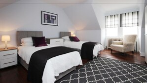 A modern bedroom with two beds, a nightstand, a chair, and a large window with blinds. - Braemount House (Paisley)