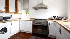 A modern kitchen with white cabinets, a stainless steel stove, a microwave, and a washing machine. - Braemount House (Paisley)