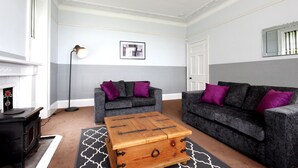 A living room with two grey sofas, a wooden coffee table, a fireplace, and a floor lamp. - Braemount House (Paisley)