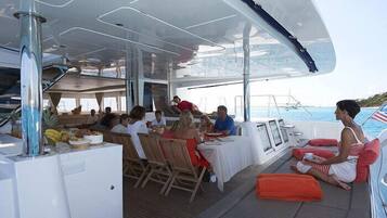 Un pont de bateau où des personnes prennent leur repas, une table de buffet et une vue sur la mer.
