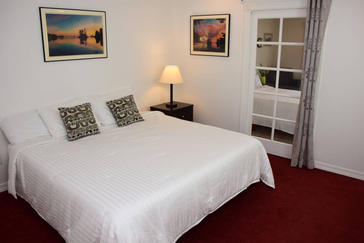 A neatly made bed with white bedding and patterned pillows, a bedside lamp, and two framed pictures on the wall.