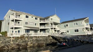 A multi-story building with balconies, located near a rocky shoreline. - Longliner Lodge and Suites (Sitka)