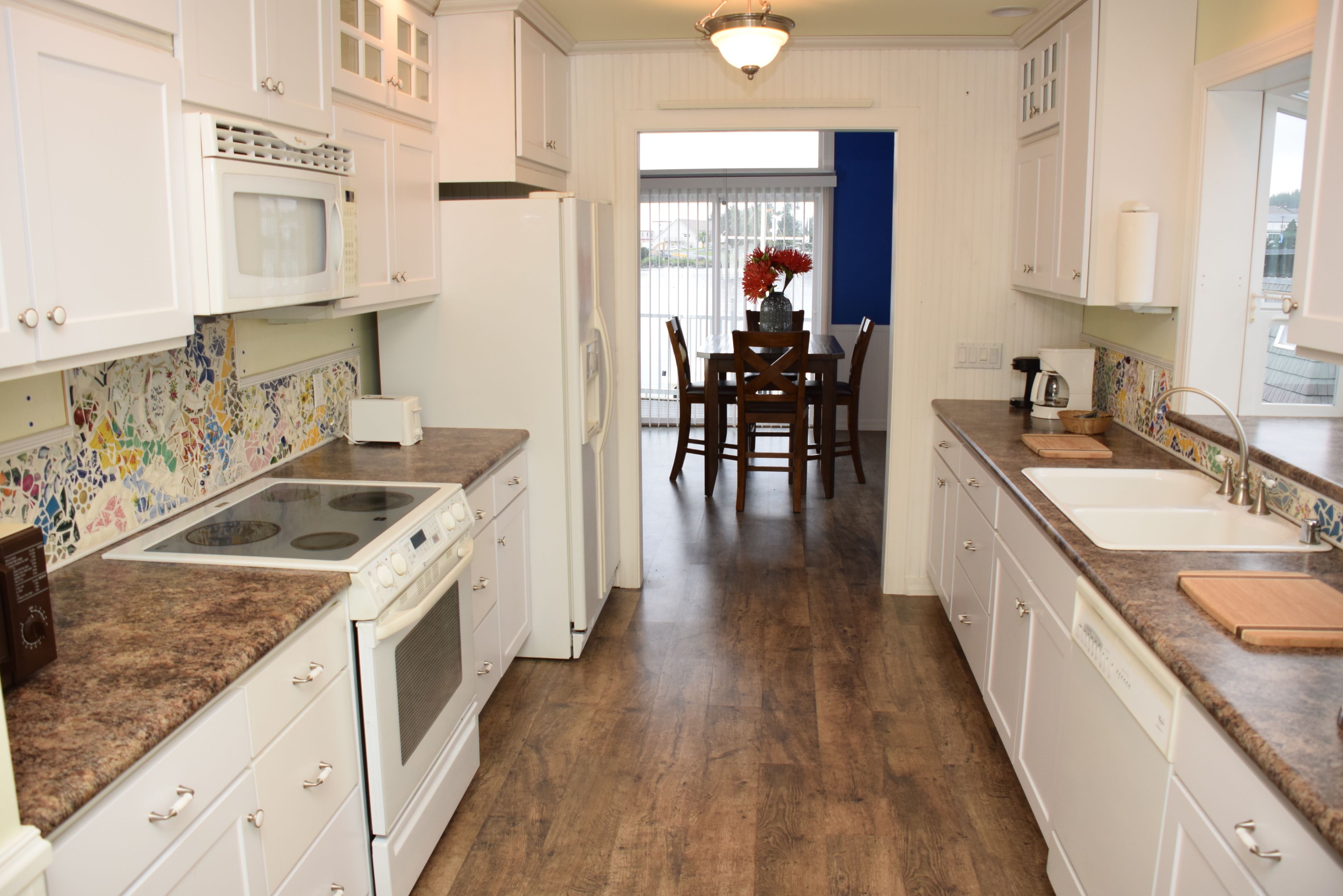 A kitchen with white cabinets, a granite countertop, a microwave, a stove, and a dining area with a table and chairs.