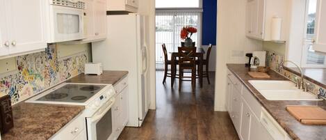 A kitchen with white cabinets, a granite countertop, a microwave, a stove, and a dining area with a table and chairs.