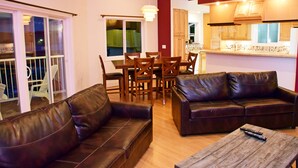 A living room with a brown leather sofa, a wooden coffee table, and a dining area with a table and chairs. - Longliner Lodge and Suites (Sitka)