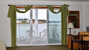 A room with a balcony, a chair, a table, and a lamp. - Longliner Lodge and Suites (Sitka)