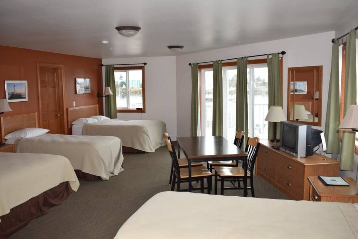 A hotel room with two single beds, a dining table with chairs, a television, and a desk with a lamp.