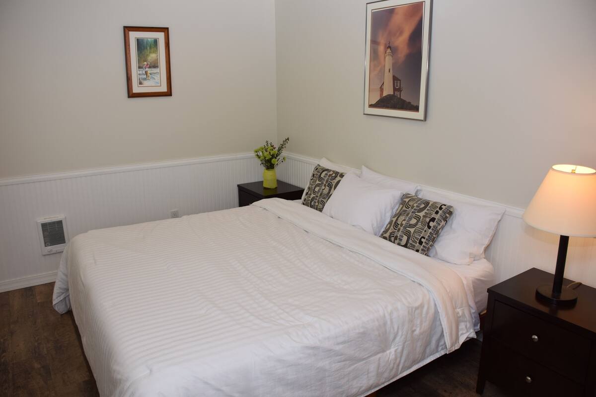 A neatly made bed with white linens, a bedside table with a lamp, and two framed pictures on the wall.
