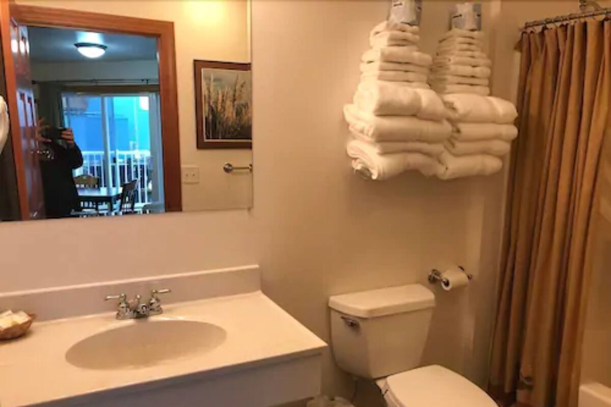 A bathroom with a sink, toilet, and a stack of towels.