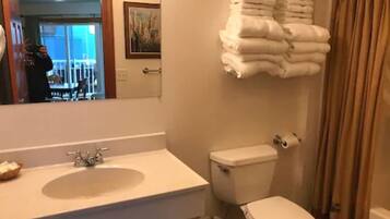 A bathroom with a sink, toilet, and a stack of towels.