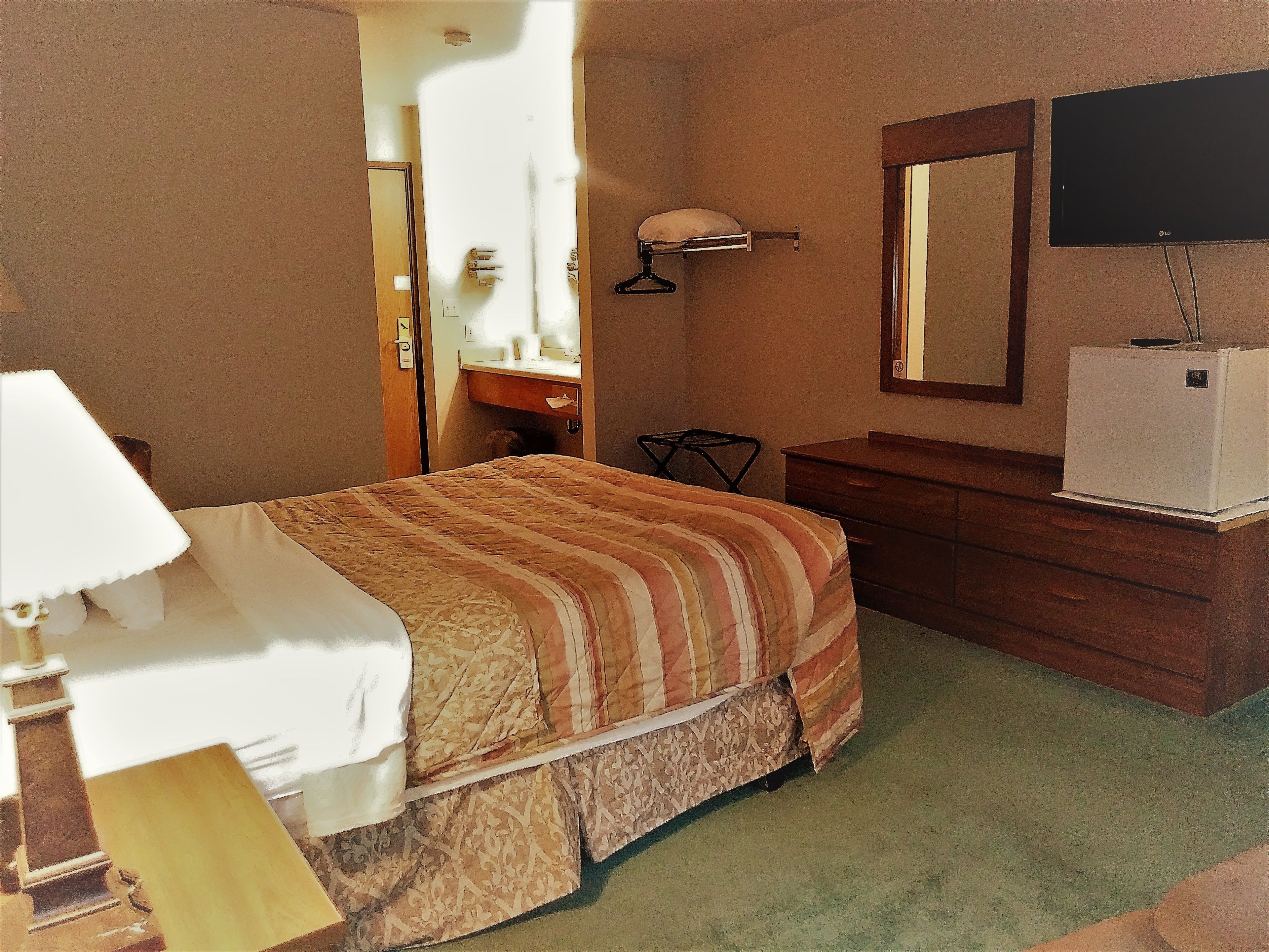 Een hotelkamer met een bed, een dressoir, een spiegel en een televisie.