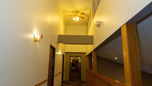 A hallway with a carpeted floor, wooden handrails, and a ceiling fan. - SunRise Inn Hotel (Mondovi)