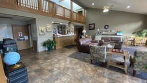 A spacious lobby with a reception desk, leather sofas, a dining area, and a high ceiling with a wooden balcony. - SunRise Inn Hotel (Mondovi)