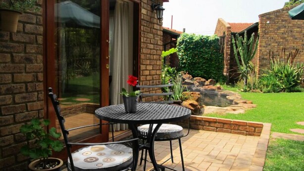A patio with a round table and chairs, a potted plant, and a view of a garden with a water feature and plants. - No 5 on Franschoek Lane (Sandton)
