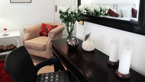 A modern living room with a beige armchair, a small side table with a red patterned pillow, a vase with white flowers, a decorative pear, and two candles on a dark wooden console. - No 5 on Franschoek Lane (Sandton)