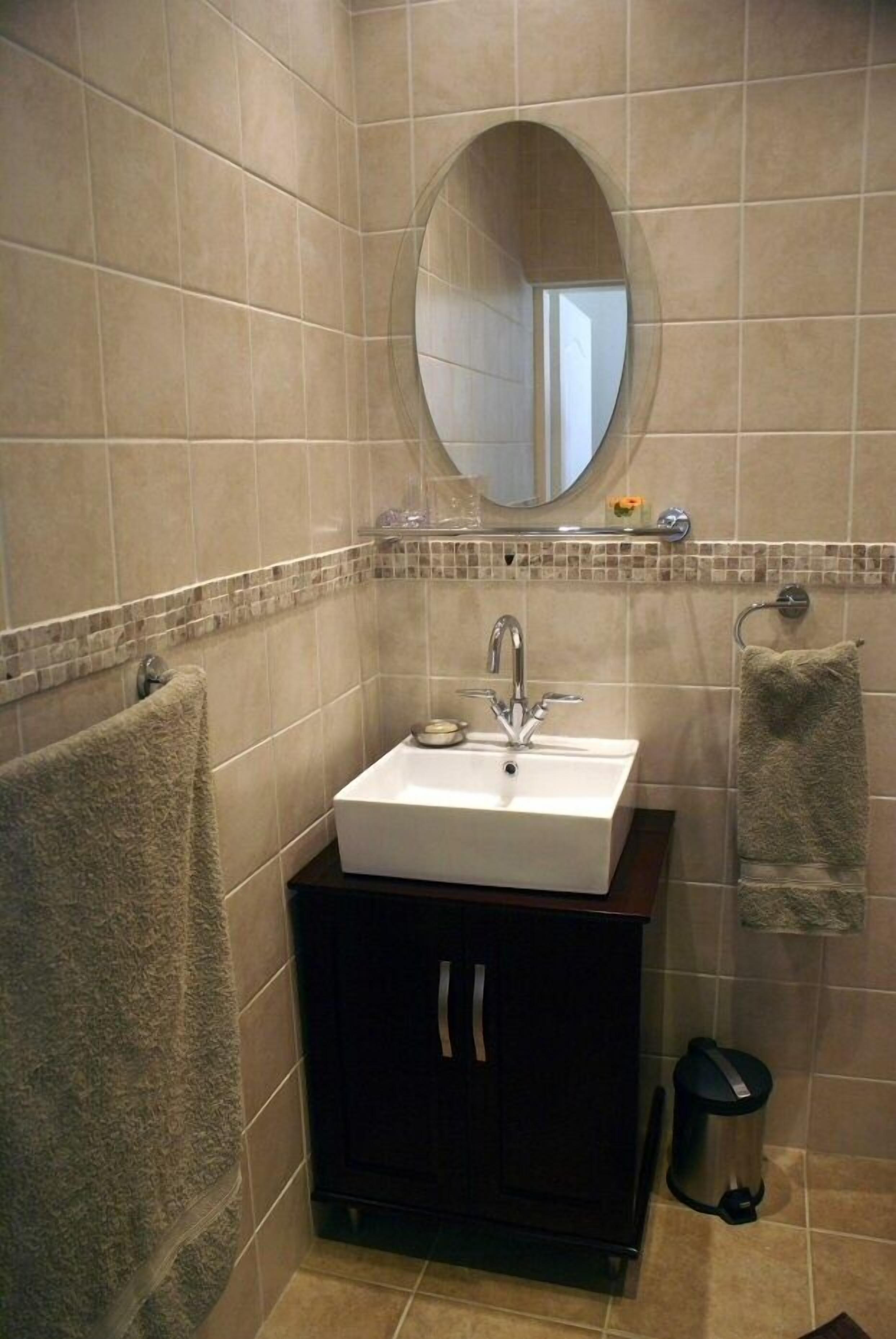 Ein Badezimmer mit einem weißen Waschbecken, einem dunklen Schrank und einem runden Spiegel.