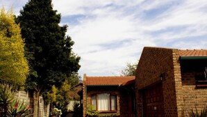 A brick house with a paved driveway, a large tree, and a clear sky. - No 5 on Franschoek Lane (Sandton)