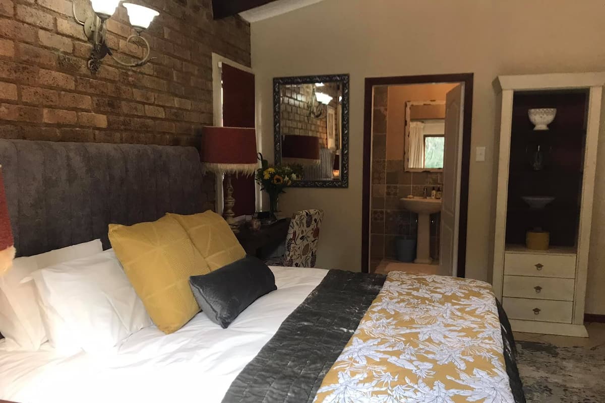 Ein Hotelzimmer mit Bett, Schminktisch, Spiegel und einem durchgegangenen Tür sichtbar liegenden Badezimmer.