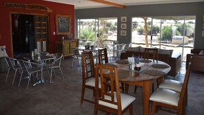Un comedor con una mesa y sillas de madera, una pared roja con un letrero, y ventanas amplias que dan a vistas del exterior.