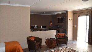 Habitación de hotel con sofá, una mesita, alfombra y una kitchenette al fondo.