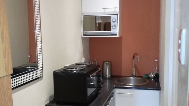 A compact kitchen with a microwave, stove, and sink. - Framesby Guesthouse (Gqeberha (Port Elizabeth))
