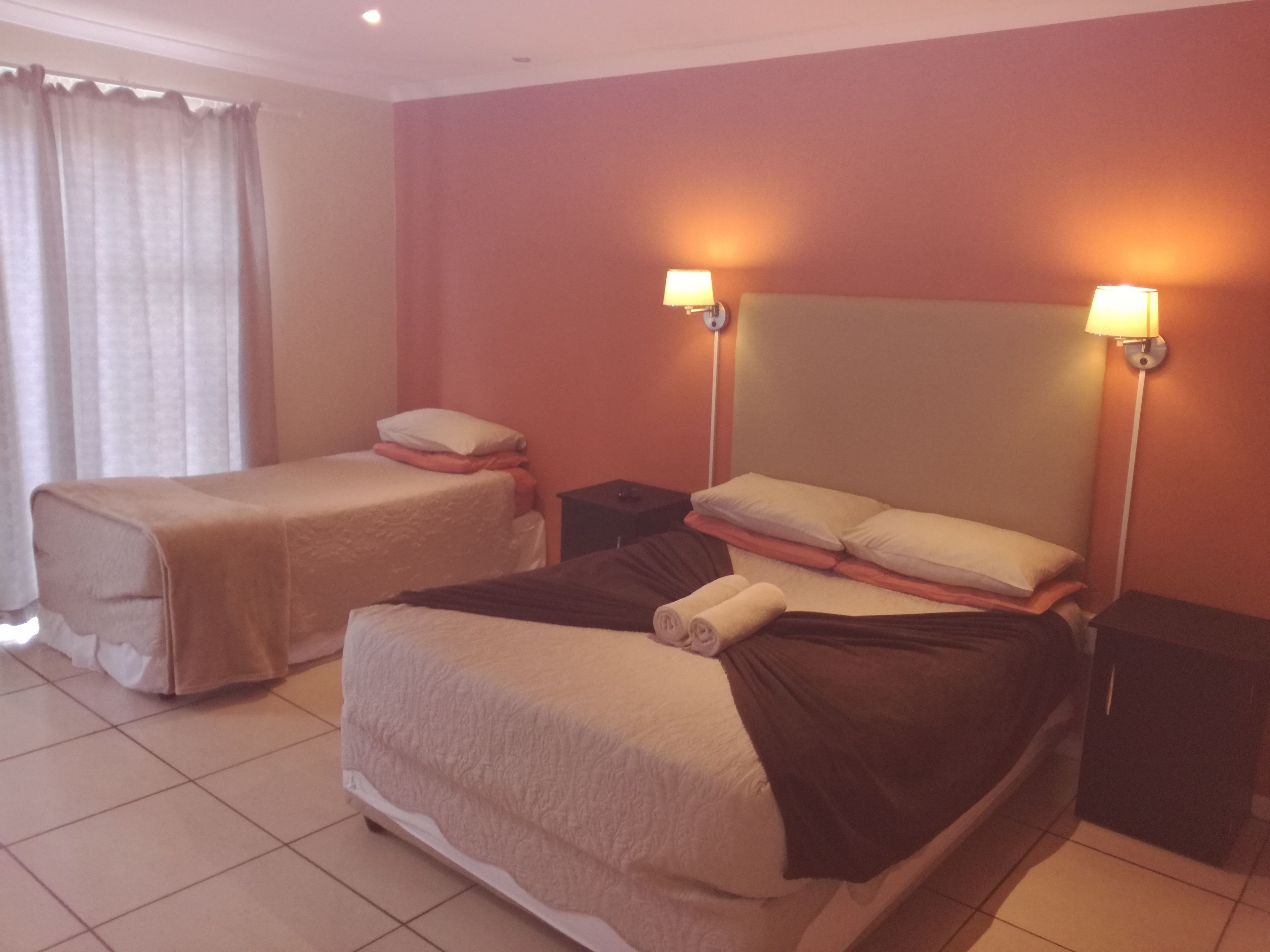 A hotel room with two single beds, a large bed, and a nightstand between them.