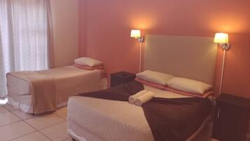 A hotel room with two single beds, a large bed, and a nightstand between them.